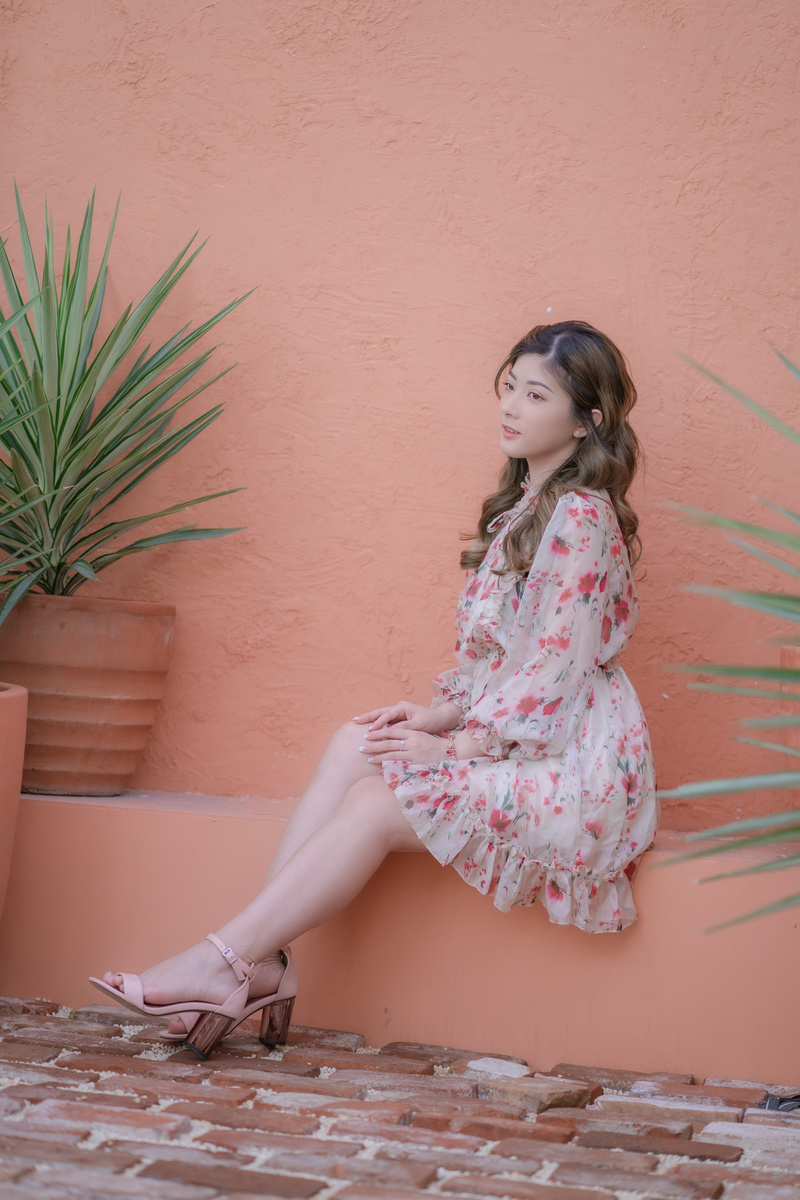 A Woman in White and Pink Floral Dress Sitting on Concrete Wall